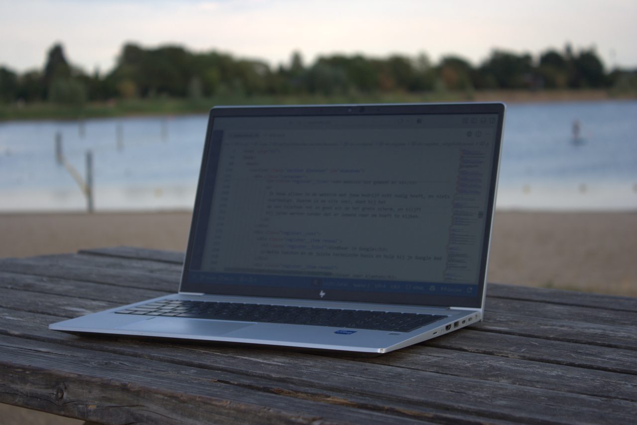 Een laptop op een picknicktafel aan het water, met een code-editor open