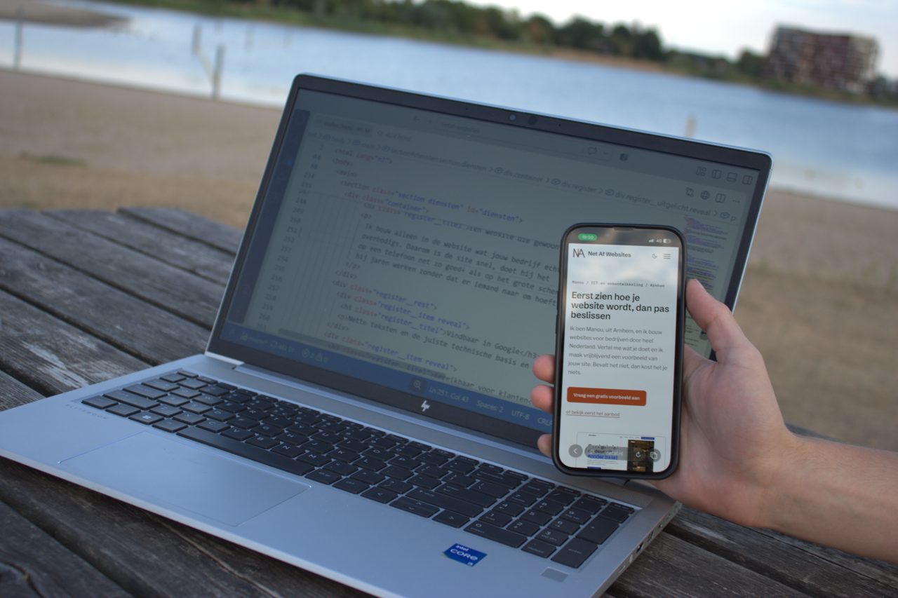 Een hand houdt een telefoon met een website erop, met op de achtergrond een laptop