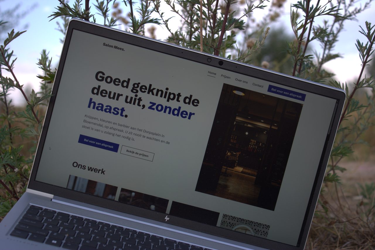 Het kapsalon-ontwerp Salon Mees open op een laptop, buiten tussen het groen